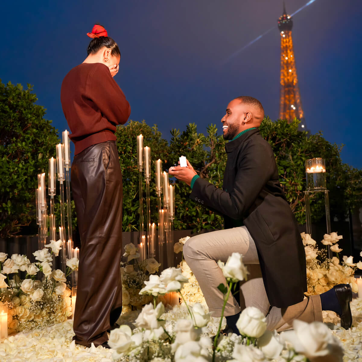 Black couple enjoying a romantic New York City proposal on a private Paris rooftop at night, surrounded by luxury floral arrangements with the Eiffel Tower twinkling in the background, captured by a professional New York City proposal photographer.