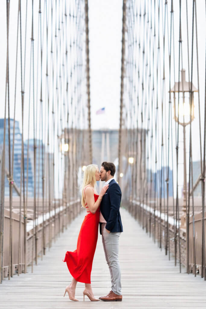 Engaged couple sharing a tender moment on the Brooklyn Bridge at sunrise, embodying the romance of NYC.