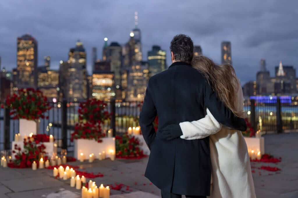 Romantic NYC engagement photo with the couple facing the dazzling Manhattan skyline from an unusual vantage point in Brooklyn Heights.