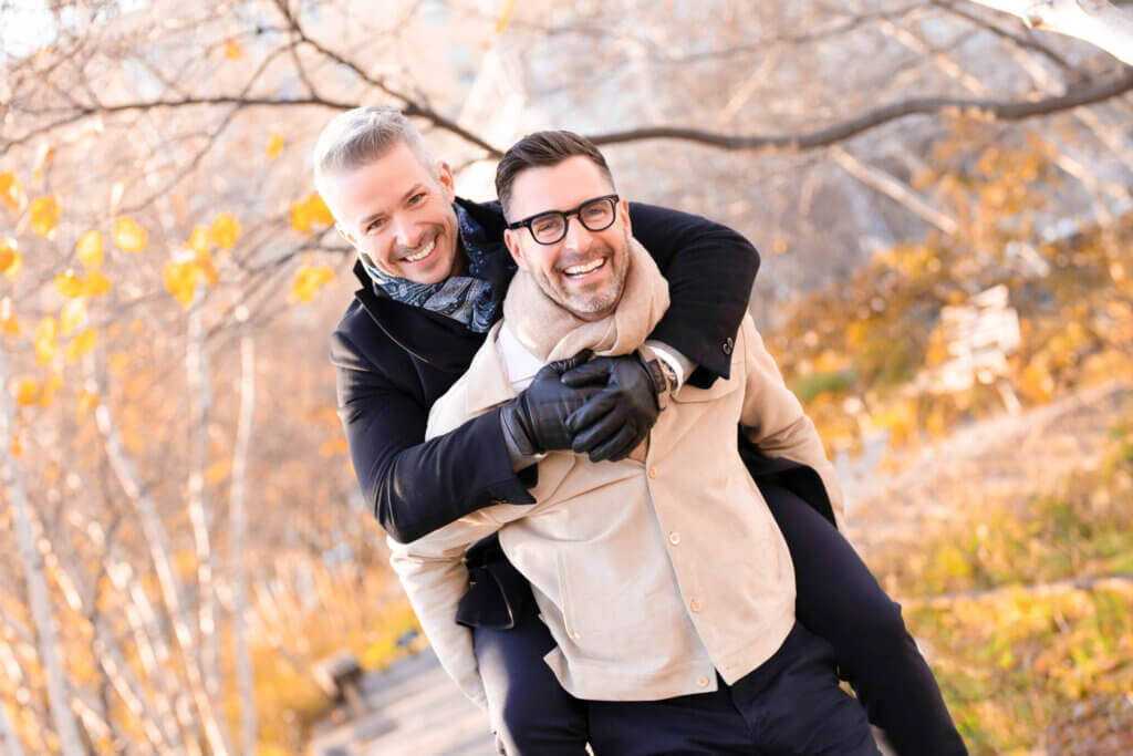 Elegant same-sex couple connecting naturally for their engagement photo session on The High Line, West Village, NYC, amidst vibrant yellow autumn leaves.