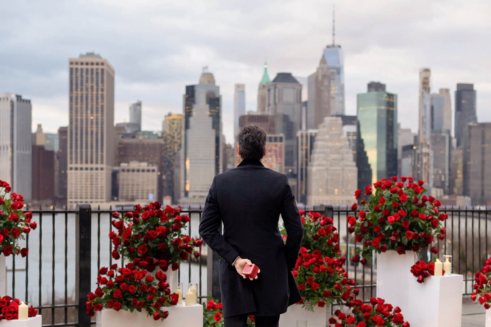 Romantic proposal in New York City: a gentleman, holding a signature red Cartier diamond ring box, is poised to propose against the mesmerizing backdrop of the Manhattan skyline.