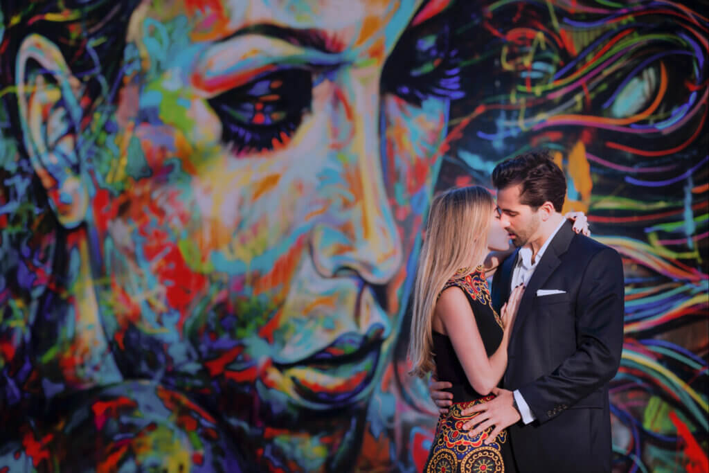 Elegant couple sharing a romantic kiss in front of a striking, colorful mural during their NYC engagement photoshoot.
