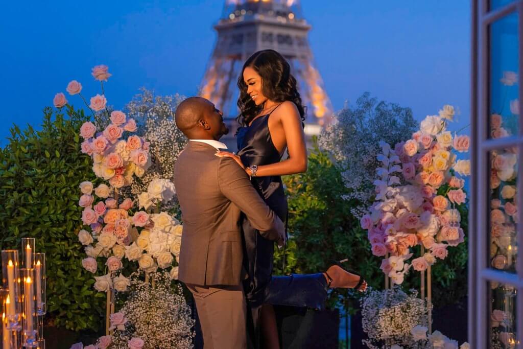 Happy couple celebrating a secret proposal amidst a divine floral setting with the Eiffel Tower sparkling in the background.