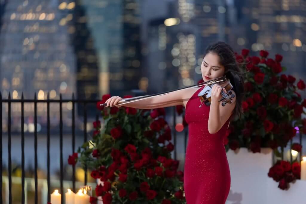 An elegant NYC Violinist dressed in red plays with divine beauty as the groom awaits, with the breathtaking NYC skyline as the backdrop.