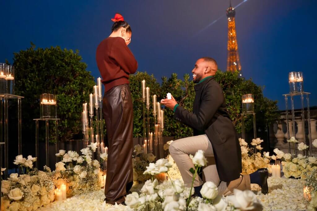 High-end NYC Photographer captures a dazzling proposal moment with the couple encircled by thousands of white rose petals and with the Eiffel Tower twinkling against a blue sky.