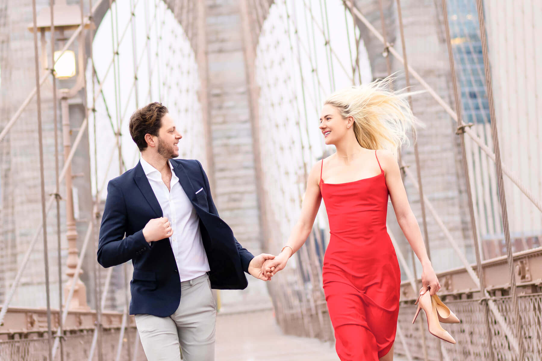 Fun-loving couple running on Brooklyn Bridge at sunrise, capturing bigger than life engagement photos.