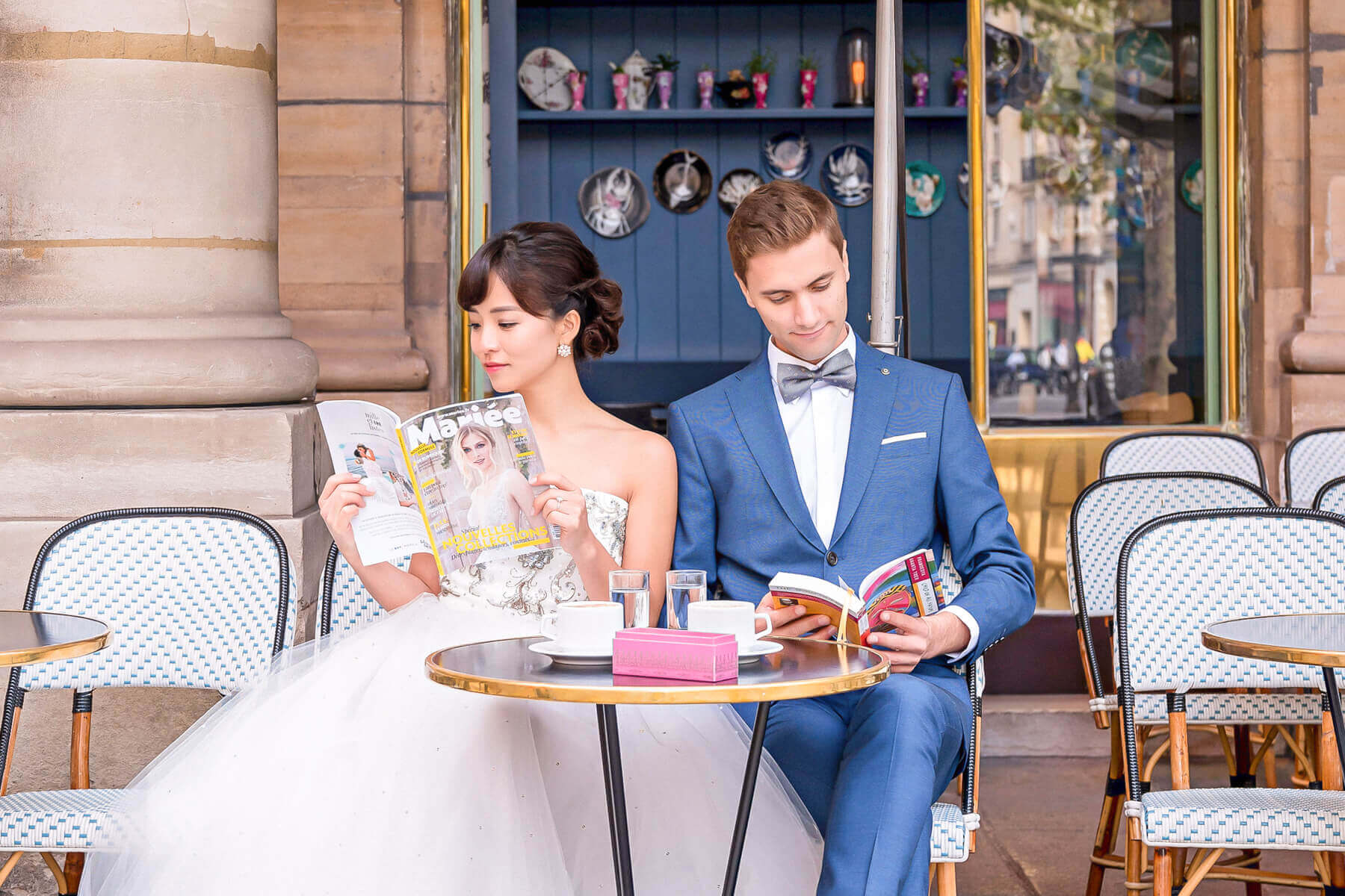 Happy couple enjoying coffee and macarons at a picturesque cafe, reading together in charming cafe engagement photos.