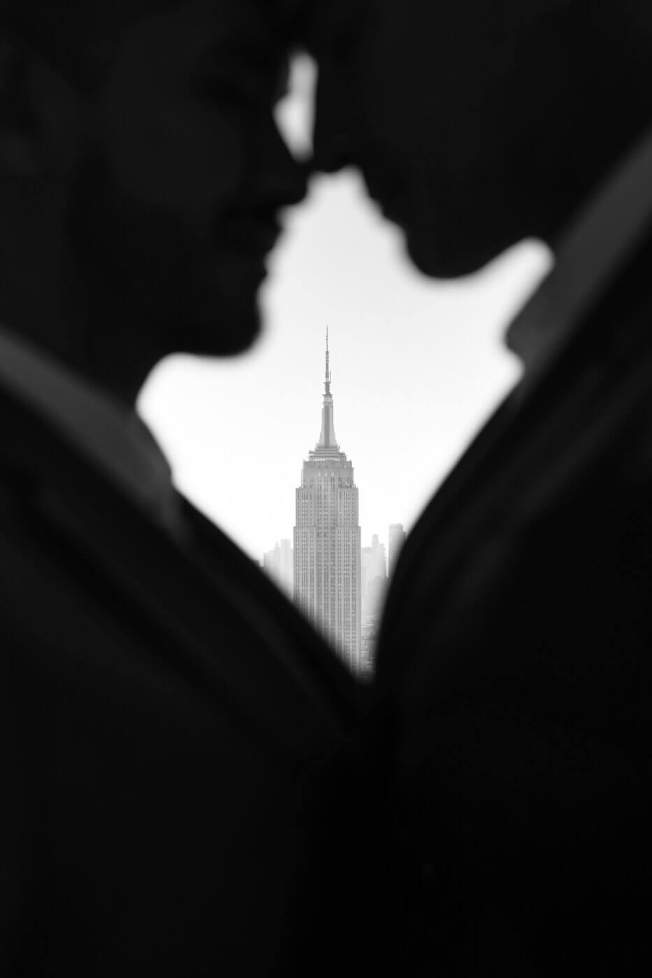 Stylish gay couple posing with the Empire State Building in between them, embodying the Big Apple in their NYC Engagement Photos.