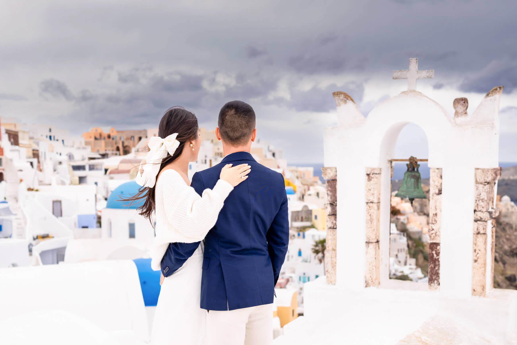 Couple embracing on iconic Santorini blue and white washed rooftops moments after getting engaged, captured by the best destination wedding photographer.