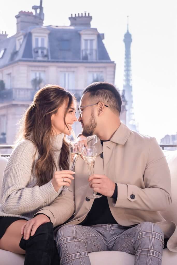 An excited couple shares a celebratory Champagne toast after their engagement in Paris. The Eiffel Tower beautifully frames their special moment, epitomizing the romance of saying 'Yes' in Paris.