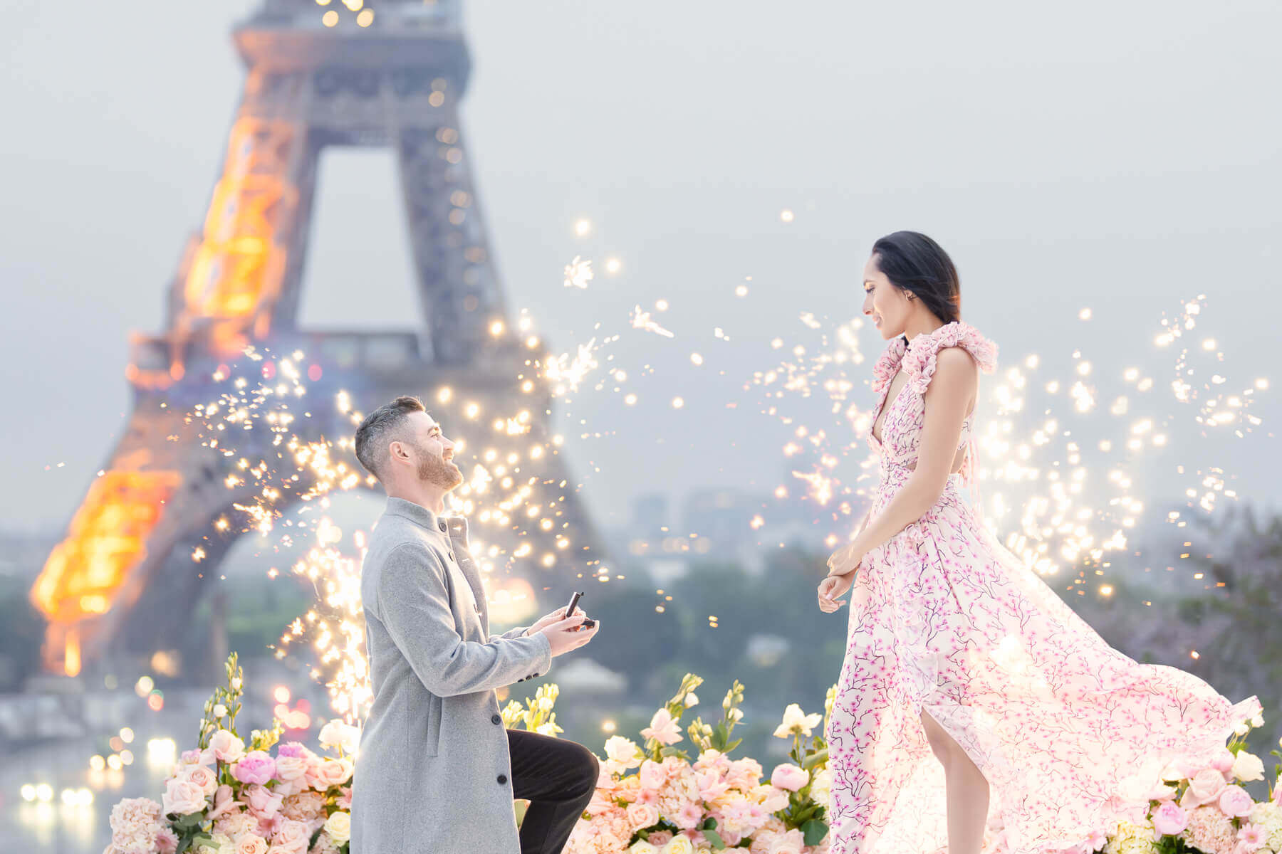 A breathtaking surprise marriage proposal in Paris, with the couple framed by fireworks fountains and the Eiffel Tower in the background, expertly planned by a premier Marriage Proposal planner.